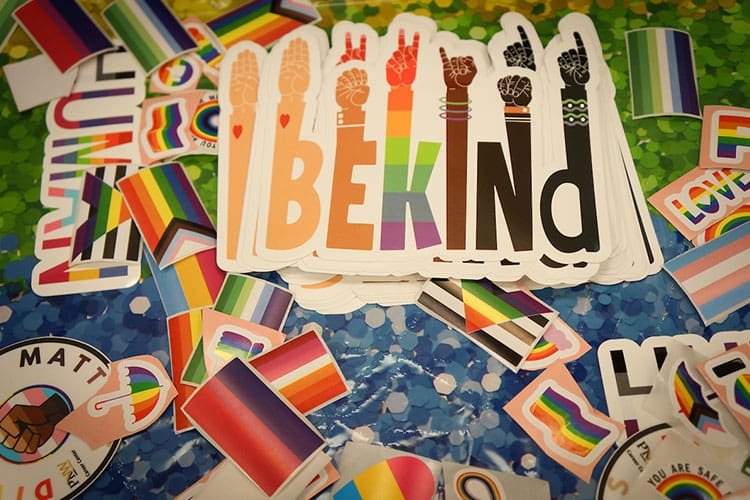 A "Be Kind" sticker sits on a pile of other pride themed stickers